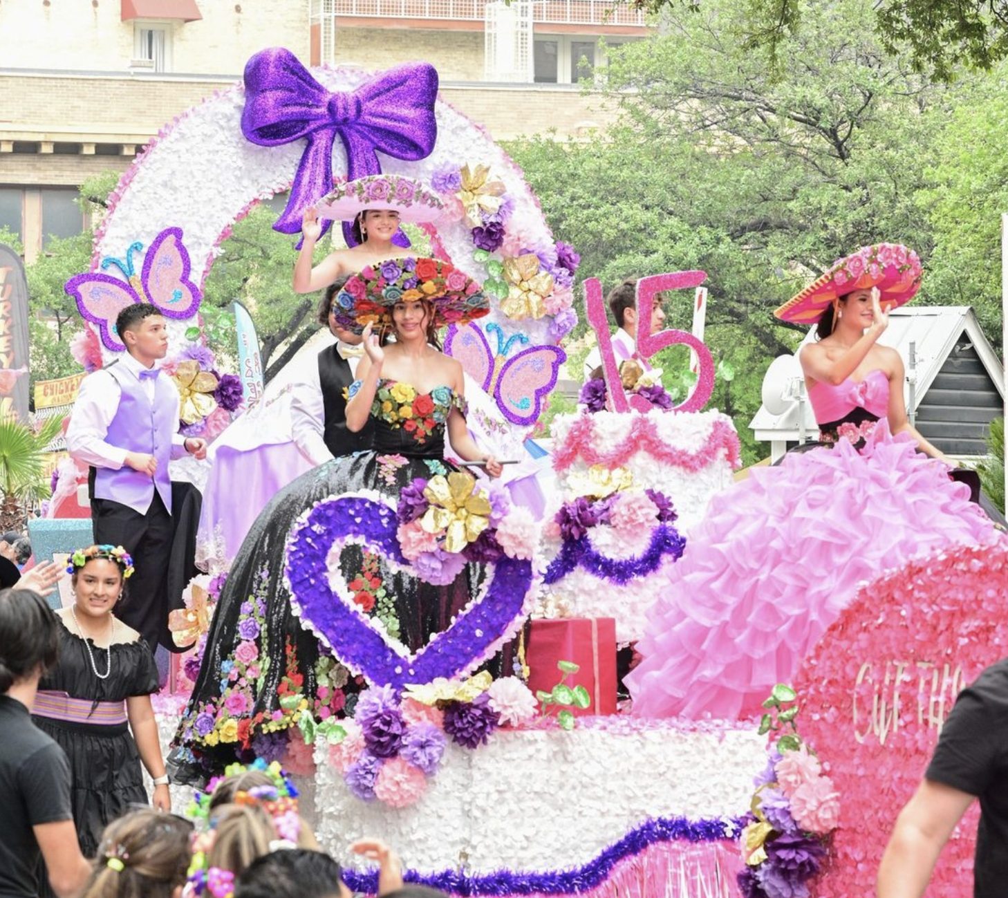 Quinceañeras in colorful gowns on a flower-covered parade float in San Antonio