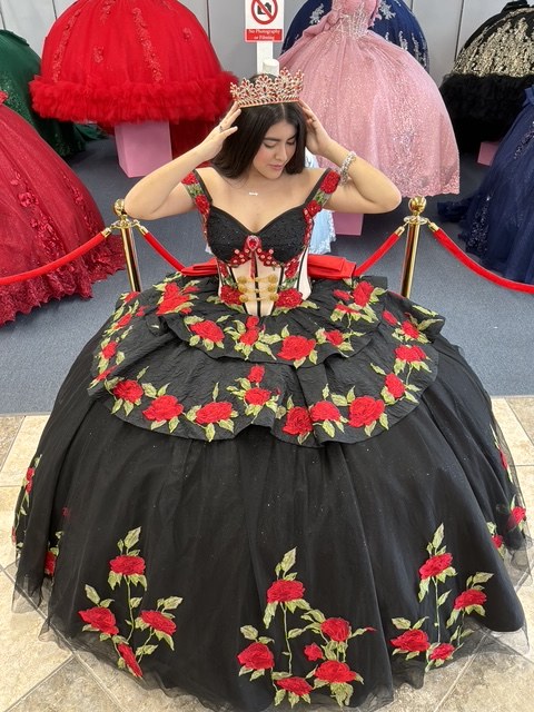 Black charro quinceañera dress embroidered with red roses, worn with a red crystal crown