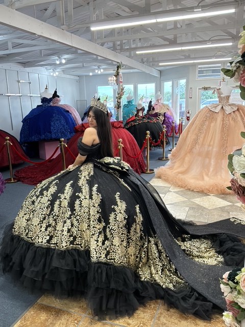 Black quinceañera ball gown with gold embroidery and ruffled tulle hem, worn in the showroom
