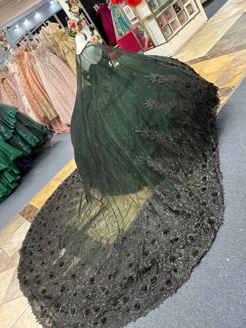 Emerald green quinceañera gown with a long embroidered glitter veil spread across the showroom floor