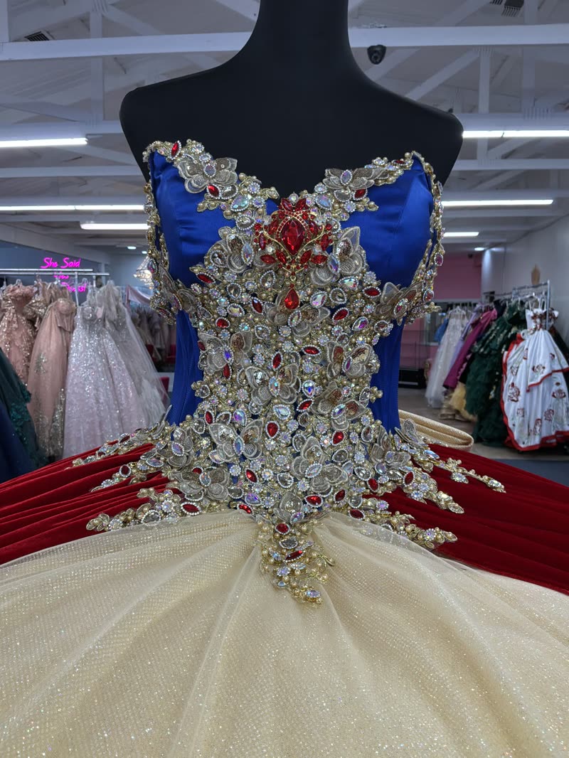 Close-up of a royal blue corset bodice covered in gold, crystal and ruby jewels above a champagne glitter skirt