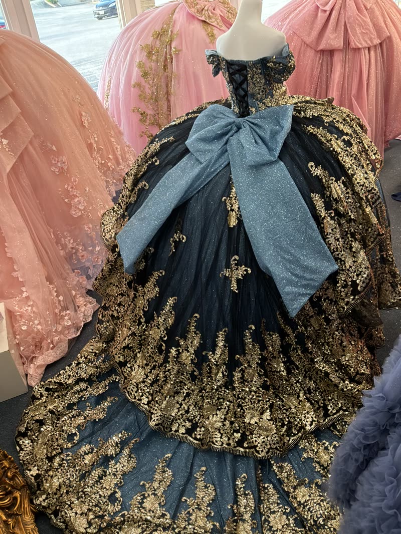 Back of a midnight navy quinceañera gown with a dusty blue glitter bow and gold-embroidered train