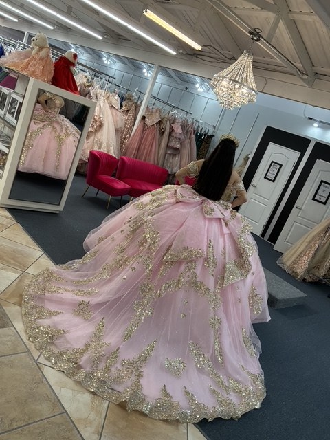 Back view of a blush pink quinceañera gown with a long gold-embroidered train in the showroom