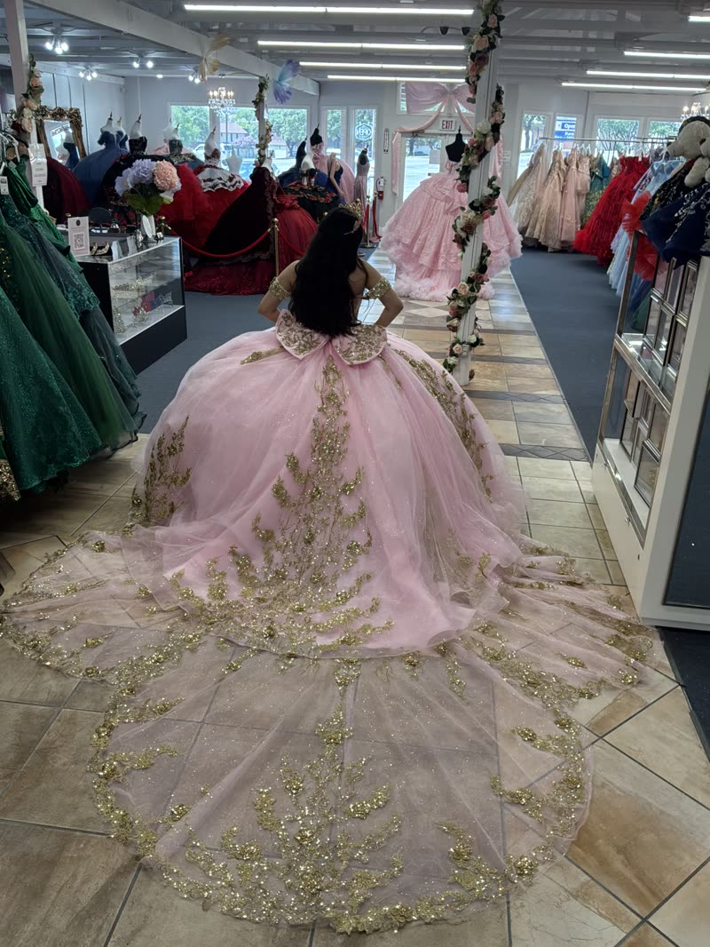 Back view of a pink quinceañera gown with a long gold sequin train sweeping the showroom aisle