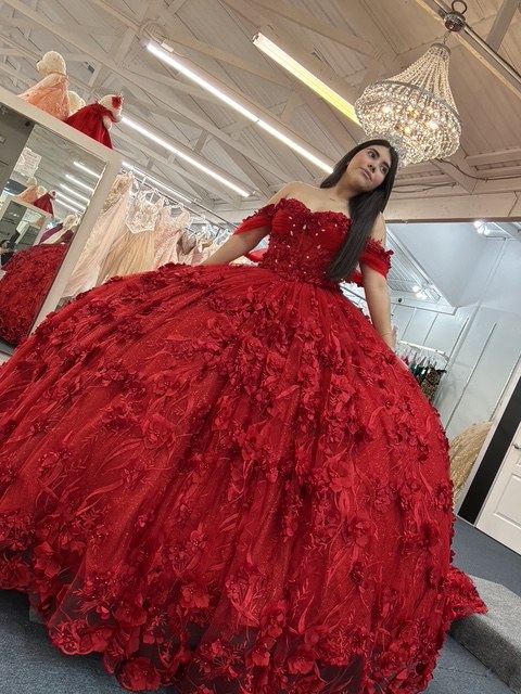 Red quinceañera ball gown covered in 3D roses and glitter tulle, worn under a chandelier