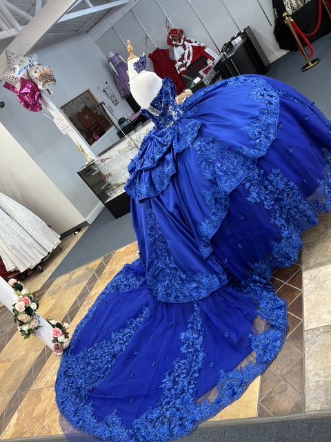 Royal blue quinceañera gown with floral lace appliqué and a sweeping train across the showroom floor