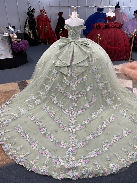 Sage green quinceañera gown with pastel 3D flowers and a satin bow, photographed from the back
