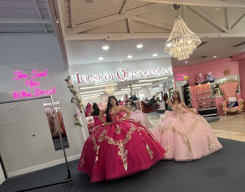 Two quinceañeras in fuchsia and blush gold-appliqué ball gowns under the chandelier at House of Quinceañeras