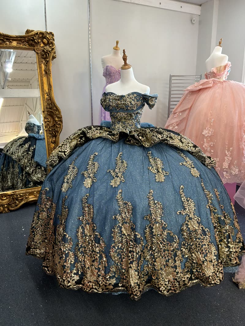 Steel blue quinceañera gown with cascading gold sequin appliqué beside a gilded mirror