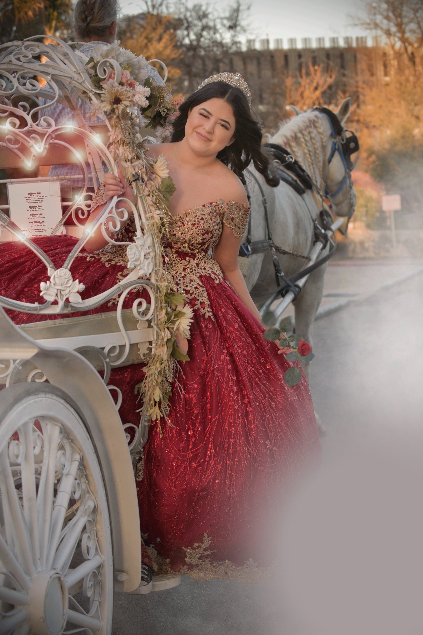 Quinceañera in a red and gold gown stepping out of a white princess carriage drawn by a white horse